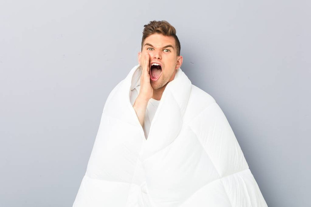 Young man holding a nordic duvet shouting excited to front. - Photo, Image