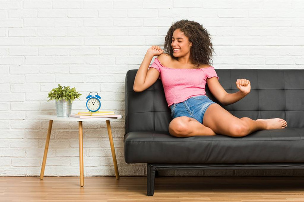 Young african american woman sitting on the sofa dancing and having fun. - Photo, Image