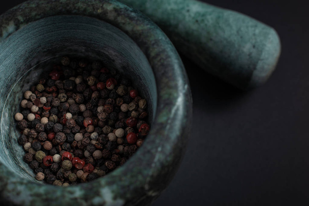 Mixture of peppercorns in a stone marble mortar of green color isolated on a black background - Valokuva, kuva