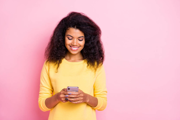 Portrait of positive cheerful black lady feel interested use her cell phone read feednews in social network account wear good looking trend outfit isolated over pastel pink color background - Zdjęcie, obraz