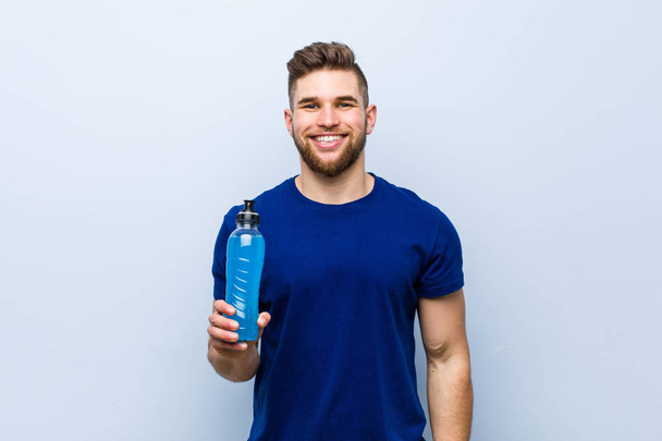 Young caucasian sportsman holding an isotonic drink happy, smiling and cheerful. - Foto, imagen