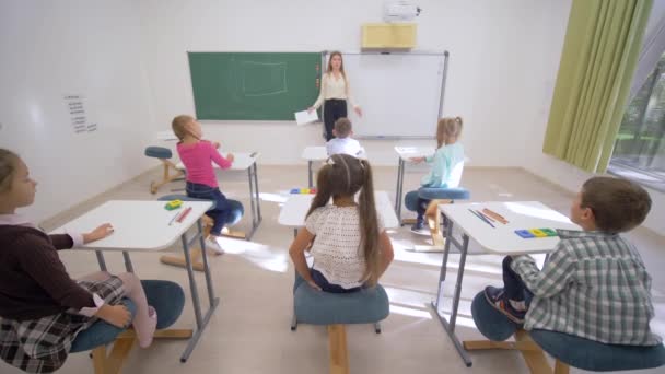 Gruppe von Schülern hebt die Hände, um im Unterricht zu antworten, während sie am Schreibtisch vor der Schultafel in der Sekundarschule sitzt - Filmmaterial, Video