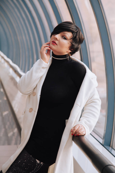 Young beautiful stylish woman in white wool coat walking down the street. Plus size short hair adult girl posing alone. - Photo, Image