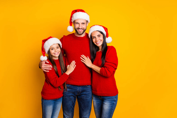 Photo of cute affectionate adorable family smiling toothily hugging each other wearing jeans denim santa cap headwear smiling toothily isolated over vivid color yellow background - Фото, изображение