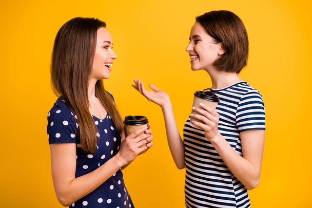 Profile photo of two amazing ladies holding hot take away coffee cups communicating with delight wear summer casual trendy dresses isolated yellow background - Foto, imagen