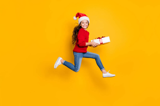Full size profile photo of crazy little lady jumping high taking giftbox from santa in x-mas midnight wear red knitted pullover and jeans isolated yellow background - Фото, изображение