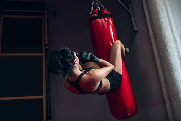 Rear view image of young woman boxer hitting a huge punching bag at a boxing studio. Sportswoman kickboxer training hard in the gym. Sport, lifestyle and people concept. - Photo, Image