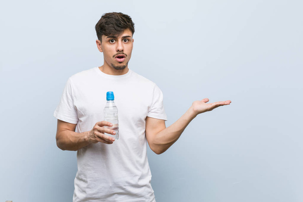 junger hispanischer Mann mit Wasserflasche beeindruckt mit Kopierplatz auf Handfläche. - Foto, Bild