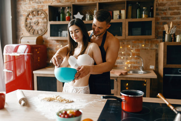 Aşk çifti iç çamaşırlarıyla mutfakta yemek pişiriyor, romantik bir sabah. Çıplak adam ve kadın evde kahvaltı hazırlıyorlar, kıyafetsiz yemek hazırlıyorlar. - Fotoğraf, Görsel