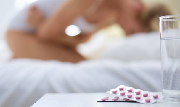 Young beautiful woman with pills lying on bed in bedroom - Φωτογραφία, εικόνα