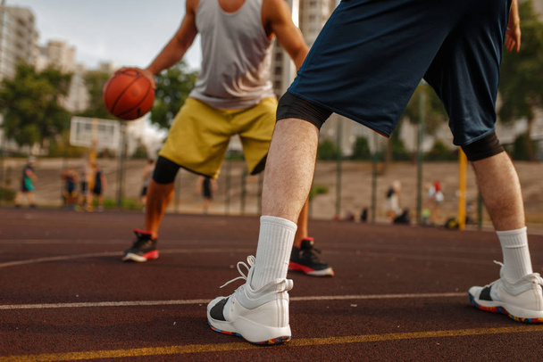 Basketbol sahasının ortasında açık sahada iki oyuncu. Spor giyim sektöründe erkek sporcular sokak topu antrenmanında oynuyor. - Fotoğraf, Görsel