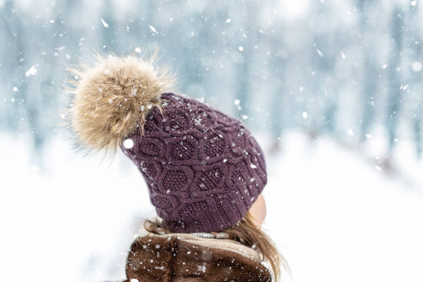 若い大人の女性の頭のクローズアップビューは、大きなふわふわの天然の毛皮のポンポンで暖かいスタイリッシュなウールニット手作りの帽子を身に着けています。寒い冬の日にシティパークや森林デュリンの雪の中を歩くと - 写真・画像