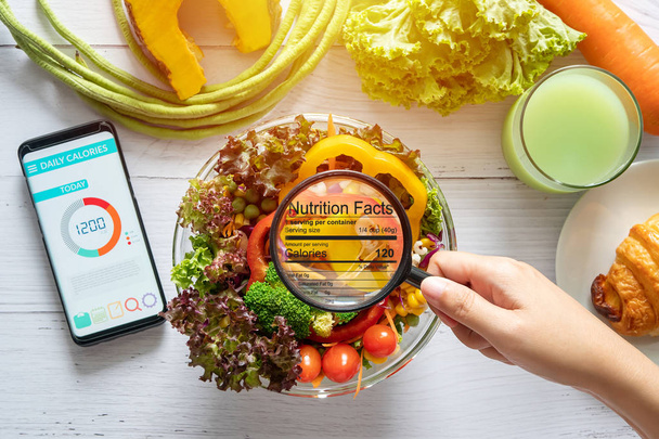 nutritional information concept. hand use the magnifying glass to zoom in to see the details of the nutrition facts from food , salad bowl - Fotoğraf, Görsel
