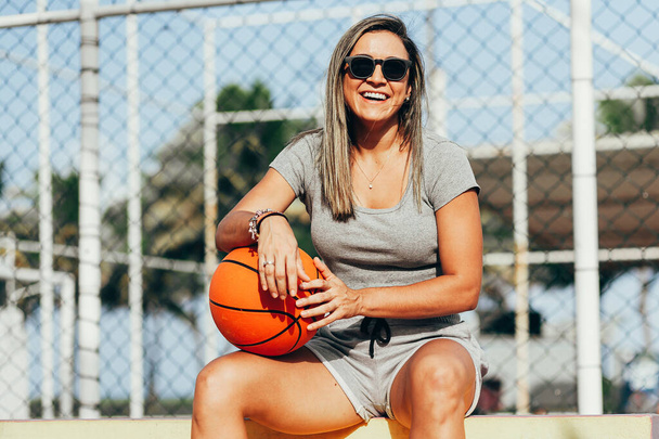 Fitness woman relaxing after workout sitting with a basketball. Woman in fitness wear sitting and relaxing during workout - Φωτογραφία, εικόνα