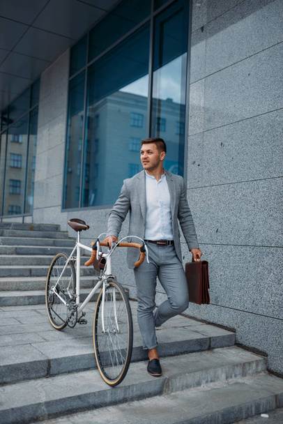 Zakenman in pak met fiets komt van de trap in het kantoorgebouw in het centrum. Zakenman rijden op eco-vervoer in de stad straat, stedelijke stijl - Foto, afbeelding