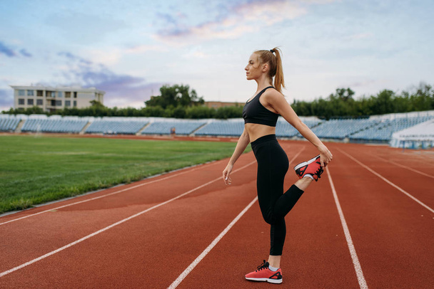 Бегунья в спортивной одежде, тренировка на стадионе. Женщина делает упражнения на растяжку перед бегом на открытой арене
 - Фото, изображение