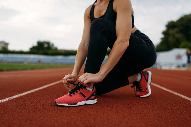 Läuferin in Sportbekleidung, schnürt ihre Schnürsenkel, trainiert im Stadion. Frau macht Dehnübungen, bevor sie auf Outdoor-Arena läuft - Foto, Bild