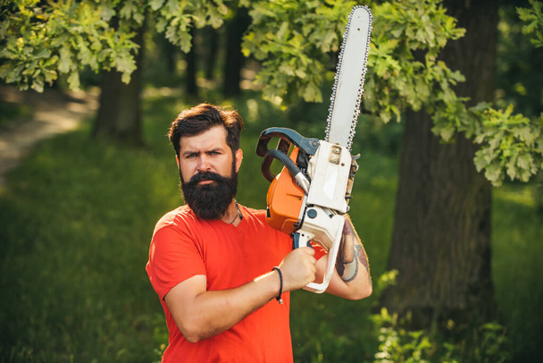 Lumberjack worker standing in the forest with chainsaw. Chainsaw. Stylish young man posing like lumberjack. Woodcutter with chainsaw on sawmill. Harvest of timber. - Foto, Bild
