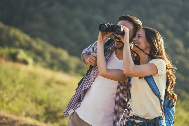 Happy couple is hiking in mountain. They are watching nature with binoculars. - Photo, Image