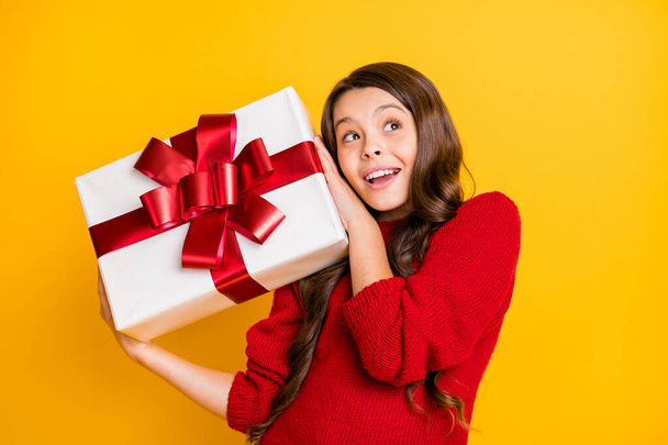 Close up photo of curious interested wavy hair child hold big gift package shake try think what she got feel anticipation newyear christmas party wear style pullover isolated yellow color background - Φωτογραφία, εικόνα