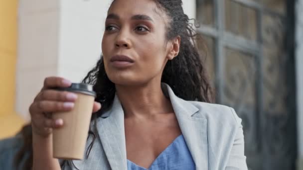 Beautiful pensive young african business woman holding takeaway coffee with both hands and thinking about something while resting in cafe - Filmmaterial, Video