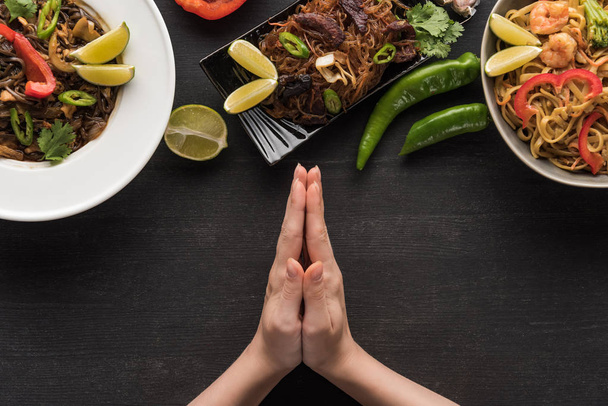 cropped view of praying hands near delicious spicy thai noodles on wooden grey surface - Photo, Image
