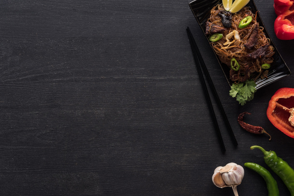 вид зверху смачної гострої тайської локшини біля паличок та інгредієнтів на дерев'яній сірій поверхні
 - Фото, зображення
