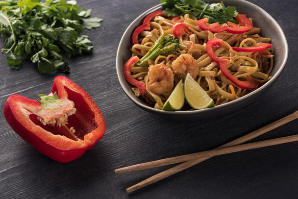 selective focus of tasty spicy seafood thai noodles near chopsticks, paprika and parsley on wooden grey surface - Foto, immagini