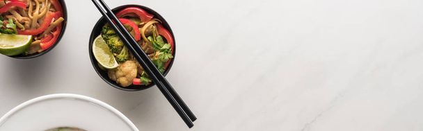 top view of delicious meat and vegetable thai noodles with chopsticks on marble grey surface, panoramic shot - Foto, afbeelding