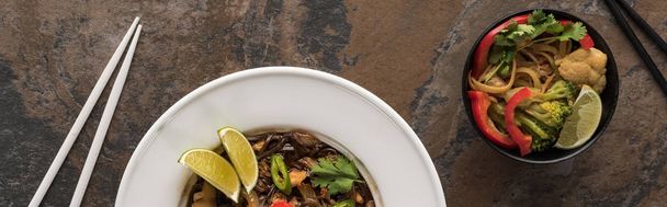 top view of thai noodles with beef and vegetables near chopsticks on stone surface, panoramic shot - Фото, изображение