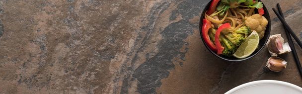 vista superior de macarrão tailandês com legumes perto de pauzinhos e alho na superfície de pedra, tiro panorâmico
 - Foto, Imagem
