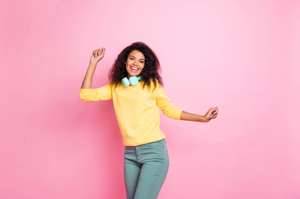 Portrait of positive cheerful funky african girl dance in night life club listen music have head phones have fun wear yellow sweater pants isolated over pink color background - Photo, image