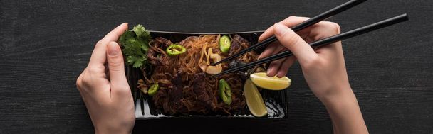 partial view of woman eating with chopsticks meat thai noodles on wooden grey surface, panoramic shot - Fotografie, Obrázek