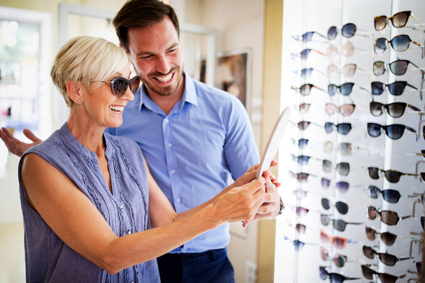 Pretty senior woman is choosing new glasses at optics store - Foto, afbeelding
