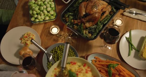 Overhead view of a group of young adult multi-ethnic male and female friends sitting around a table holding dishes and serving Thanksgiving dinner at home together - Imágenes, Vídeo