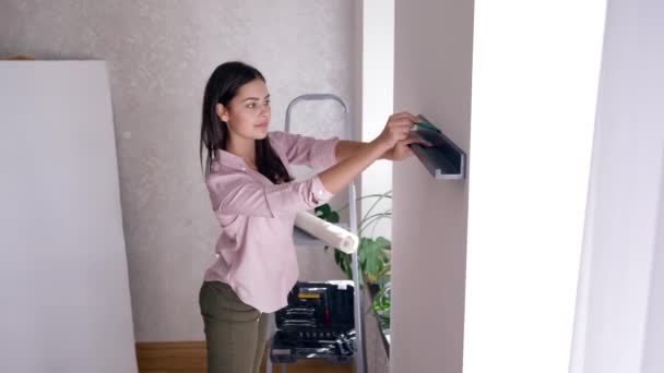 repair apartment, lovely woman does redecorating and hangs shelf on wall during renovation of home - 映像、動画