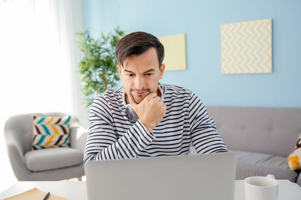 Thoughtful man working on laptop at home - Фото, зображення