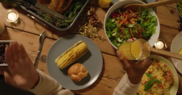 Overhead view of the hands of a group of young adult multi-ethnic male and female friends sitting at a table at home set for Thanksgiving dinner making a toast with glasses of orange juice - Záběry, video