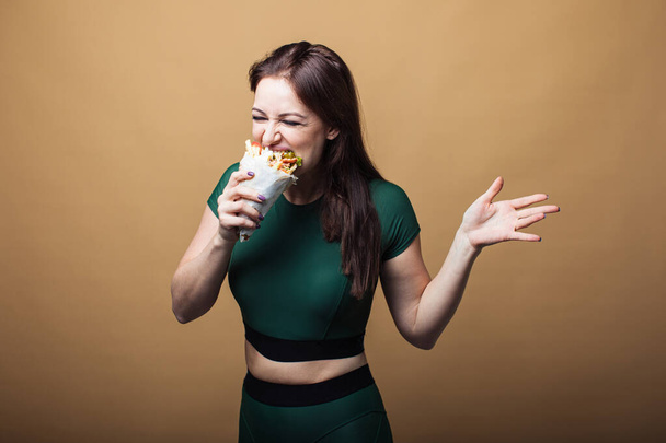 Close up of hungry girl with opened mouth, holding and eating big hamburger. Pretty woman with beautiful hairstyle and red lips. Concept of fast food - Фото, изображение