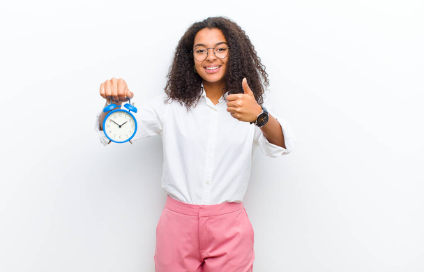 young pretty black woman with an alarm clock against white wall - Foto, afbeelding