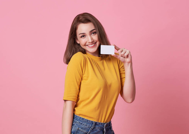 Portrait d'une jeune femme en chemise jaune montrant la carte de crédit et regardant loin l'espace de copie isolé sur fond rose
. - Photo, image