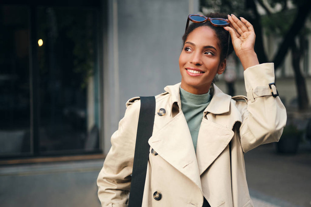 Portrait de jolie fille afro-américaine décontractée en trench coat regardant joyeusement vers l'extérieur
  - Photo, image