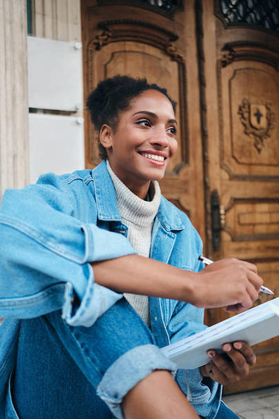 Fille étudiante afro-américaine décontractée joyeuse en veste de denim avec ordinateur portable étudiant joyeusement en plein air
  - Photo, image