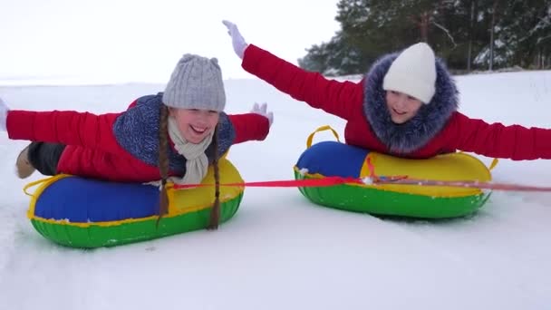 Childrens Christmas holidays outdoors. Happy children have fun riding snow saucer and laugh on snowy winter road on winter frosty day. Teens play on sled in winter field and smile. Games in fresh - Footage, Video