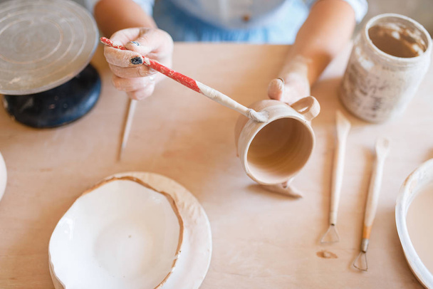 Töpferin bemalt einen Topf, Töpferwerkstatt. Frau beim Formen einer Schüssel. Handgefertigte Keramikkunst, Geschirr aus Ton - Foto, Bild