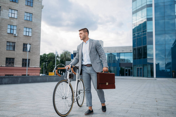 Uomo d'affari in giacca e cravatta con valigetta e bicicletta in centro. Persona d'affari a cavallo del trasporto ecologico sulla strada della città
 - Foto, immagini