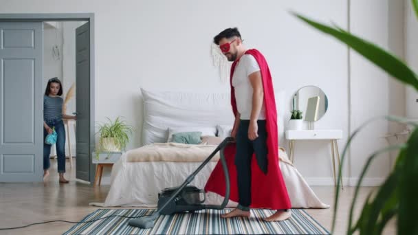 Husband in super hero costume vacuuming floor when wife coming home then running - Πλάνα, βίντεο