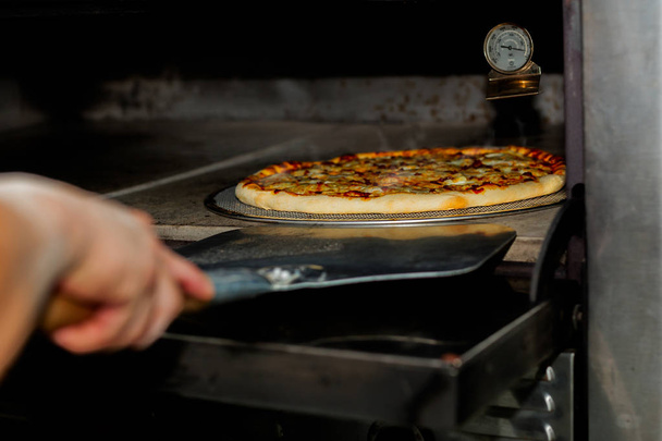 シェフはピザのシャベルでオーブンからピザを取る装置. - 写真・画像