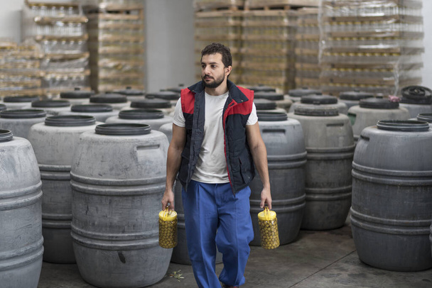 Man with bottles full of green olives walking in factory - Photo, image