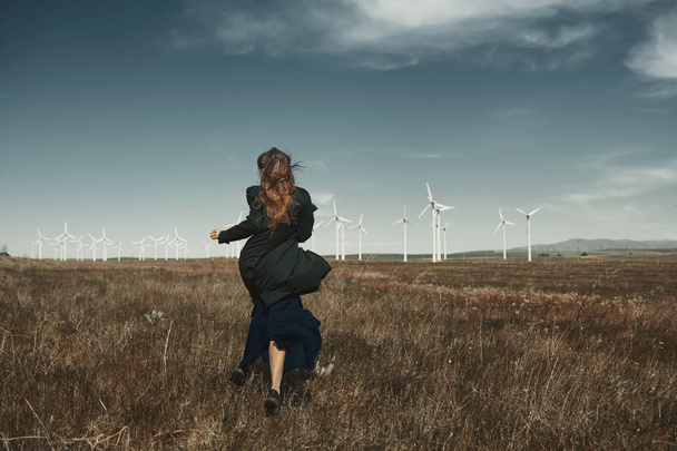 Woman with long tousled hair next to the wind turbine with the w - Photo, Image